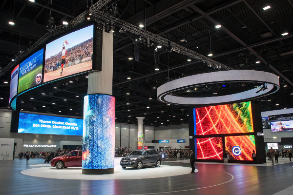 Auto exhibition featuring circular LED display, cylindrical LED screen, and rectangular displays surrounding vehicles